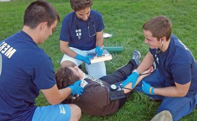 三名医疗紧急反应小组成员在训练演习中协助一名摔倒的学生